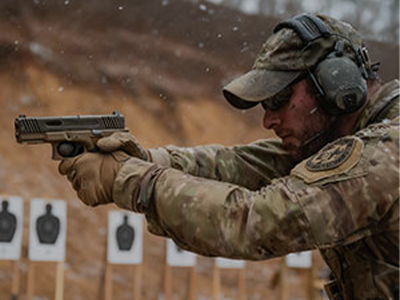 A shooting enthusiast in camouflage wearing a tactical communication headset while practicing at an outdoor shooting range