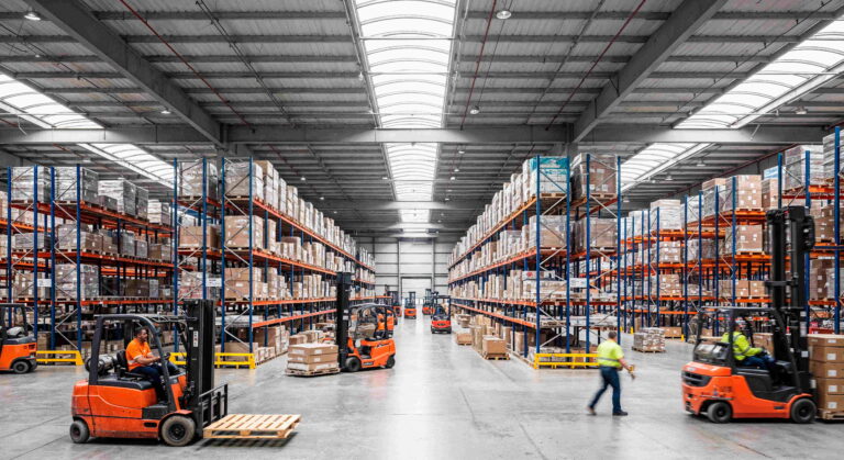 A warehouse interior with forklifts and tall shelving racks, where many workers are engaged in logistics tasks while using Bluetooth wireless communication accessories.