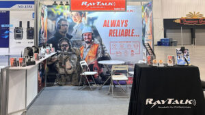 Booth at IWCE 2025 showcasing headsets, earpieces, and speaker microphones for radio communication